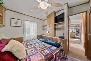 Bedroom featuring wood walls, multiple windows, ornamental molding, a wainscoted wall, and a ceiling fan
