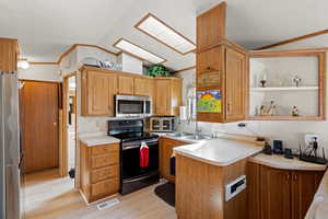 Kitchen with lofted ceiling, light countertops, a peninsula, stainless steel appliances, and ornamental molding