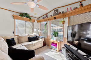 Living area featuring wooden walls, crown molding, carpet floors, a ceiling fan, and lofted ceiling