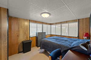 Carpeted bedroom featuring multiple windows, wooden walls, and a paneled ceiling