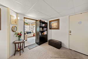 Foyer entrance with carpet flooring, a drop ceiling, and a ceiling fan