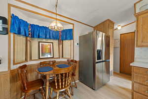 Dining room featuring light wood-type flooring, hanging lights, and a wainscoted wall