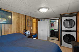 Bedroom featuring a closet, light colored carpet, stacked washer / dryer, a paneled ceiling, and wood walls