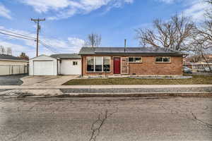 View of front of house featuring brick siding, solar panels, driveway, a garage, and a shingled roof