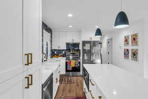 Kitchen featuring white cabinetry, stainless steel appliances, hanging light fixtures, dark wood-type flooring, and decorative backsplash