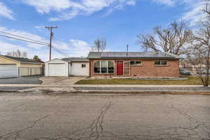 Single story home featuring roof mounted solar panels, brick siding, concrete driveway, and a shingled roof