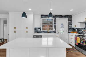 Kitchen with stainless steel appliances, pendant lighting, white cabinetry, light stone countertops, and dark wood-type flooring