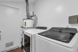Laundry room featuring dark wood-style floors, strapped water heater, and independent washer and dryer