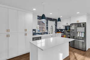 Kitchen with stainless steel appliances, white cabinets, decorative light fixtures, light stone counters, and dark wood-style flooring