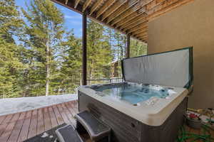 Wooden terrace with a hot tub and view of wooded area