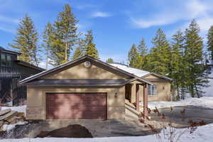 View of front of property with stone siding, a garage, stucco siding, and driveway
