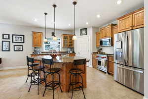 Kitchen with stainless steel appliances, a center island, dark stone counters, wood finish cabinetry, and decorative light fixtures