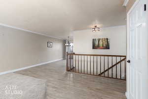 Spare room with light wood finished floors, ornamental molding, a chandelier, and a textured ceiling