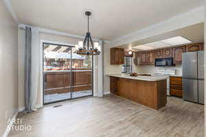 Kitchen featuring freestanding refrigerator, light countertops, white electric range, a chandelier, and a peninsula