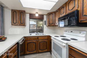 Kitchen with white electric range oven, light countertops, dishwasher, light wood-type flooring, and wood finish cabinets