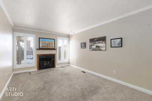 Unfurnished living room with carpet, a fireplace with flush hearth, ornamental molding, and a textured ceiling