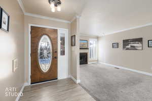 Entrance foyer with ornamental molding, a fireplace with flush hearth, light wood-style floors, and a textured ceiling