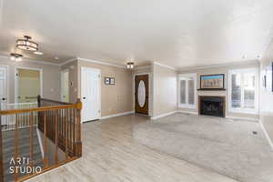 Foyer entrance featuring a fireplace with flush hearth, ornamental molding, light wood-style flooring, and a textured ceiling