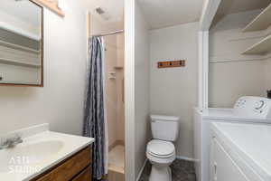 Bathroom featuring vanity, a textured ceiling, a shower stall, and washing machine and dryer