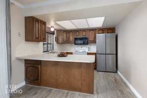 Kitchen with freestanding refrigerator, white range with electric cooktop, light countertops, black microwave, and light wood-style floors