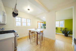 Dining room featuring light wood-type flooring, healthy amount of natural light, and lofted ceiling with beams