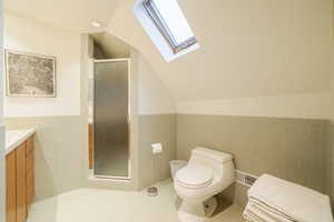 Bathroom featuring tile walls, a wainscoted wall, vanity, a shower stall, and vaulted ceiling