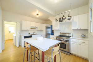 Kitchen with stainless steel appliances, white cabinetry, light countertops, and a kitchen bar