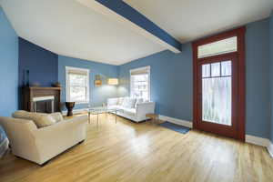 Living room with light wood-style flooring, beam ceiling, and a fireplace