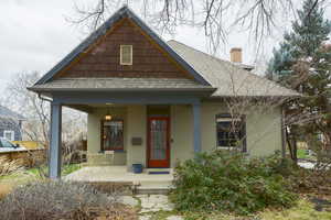 View of front of property with a porch, a shingled roof, brick siding, and a chimney