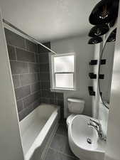 Bathroom with a textured ceiling, dark tile patterned floors, and bathing tub / shower combination