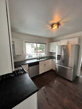 Kitchen featuring stainless steel appliances, dark countertops, white cabinetry, decorative backsplash, and dark wood-style floors