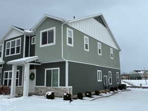 View of snowy exterior featuring stone siding, board and batten siding, and stucco siding
