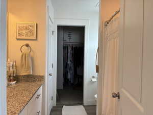 Full bathroom with vanity, curtained shower, a walk in closet, and dark wood-style flooring