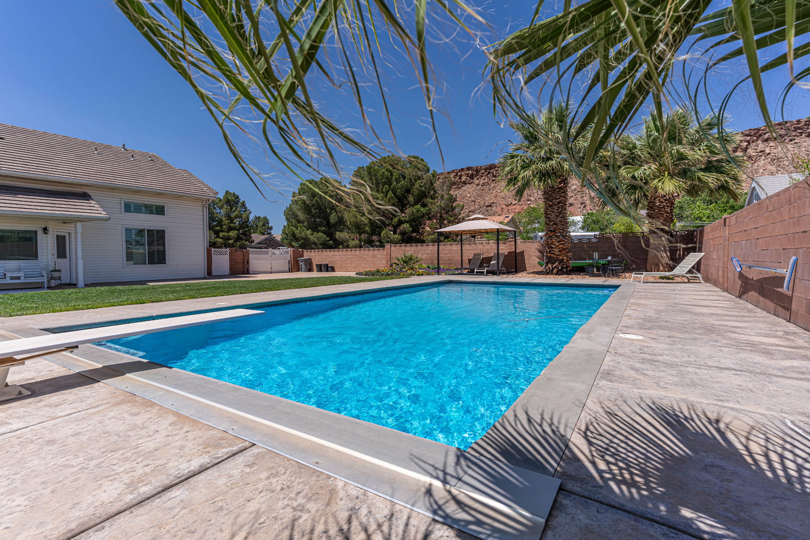 View of swimming pool featuring a gazebo, patio surround, a fenced backyard, and a diving board