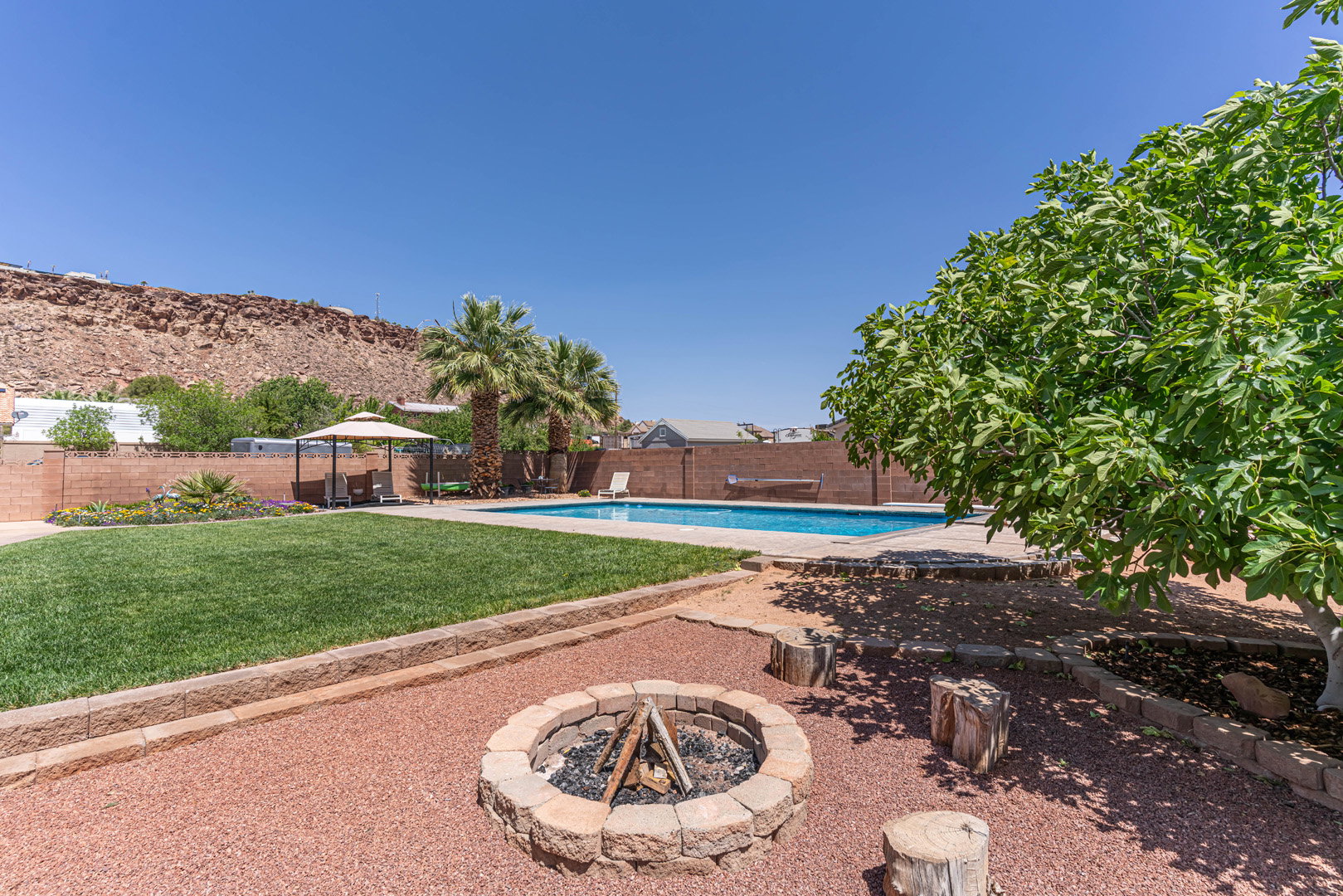 View of pool featuring patio surround, a gazebo, a fenced backyard, and an outdoor fire pit