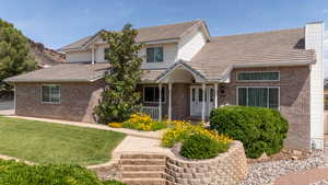 View of front of house featuring brick siding, a front yard, covered porch, and a tile roof
