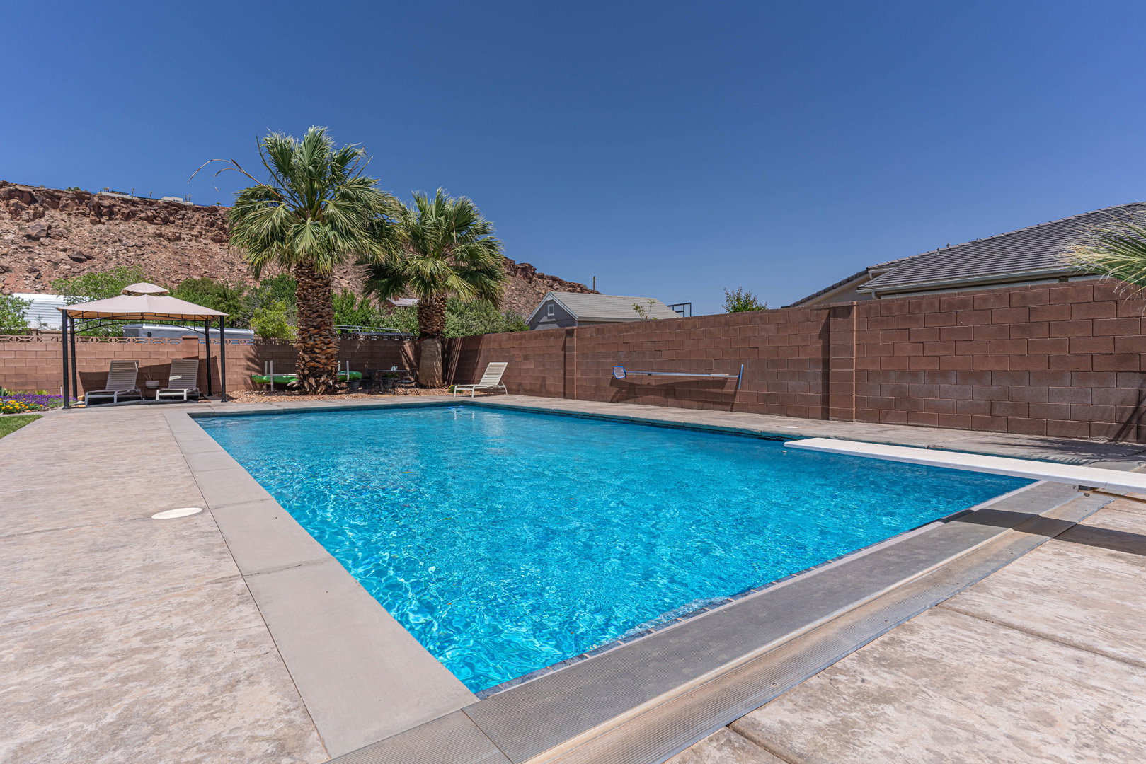 View of swimming pool with a fenced backyard, patio surround, a gazebo, and a diving board