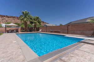 View of swimming pool with a fenced backyard, patio surround, a gazebo, and a diving board