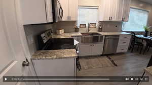 Kitchen with white cabinetry, stainless steel appliances, light stone counters, and wood finished floors