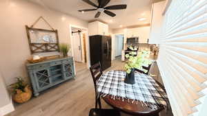 Dining area with a barn door, light wood-type flooring, a ceiling fan, and recessed lighting