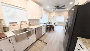 Kitchen with stainless steel appliances, white cabinetry, light stone countertops, light wood-style flooring, and a ceiling fan