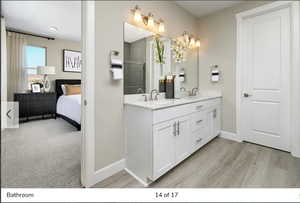 Ensuite bathroom with double vanity, light wood finished floors, and a shower stall
