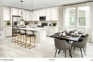 Kitchen with a breakfast bar area, stainless steel appliances, white cabinetry, an island with sink, and light wood-style floors