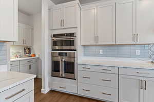 Kitchen with stainless steel double oven, tasteful backsplash, and white cabinetry