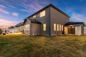 Rear view of house featuring a storage shed, a patio area, and stucco siding at twilight