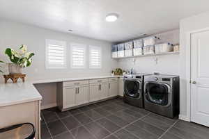 Laundry area featuring washer and clothes dryer, dark tile patterned flooring, a textured ceiling, and cabinet space. Could easily double as craft, sewing, giftwrap or homework room.