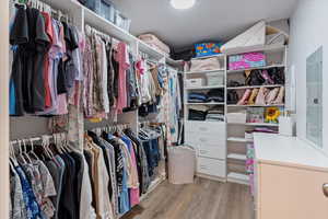 One of two total walk-in closets in the primary bedroom with light wood-style floors and cstom drawers