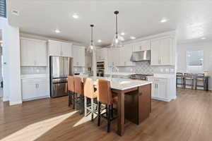 Kitchen with a center island with sink, stainless steel appliances, pendant lighting, dual tone cabinets, and a breakfast bar