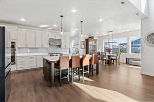 Kitchen with decorative light fixtures, dual tone cabinets, a breakfast bar area, an island with sink, and freestanding refrigerator
