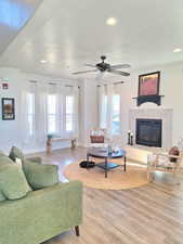 Living room featuring light wood finished floors, a premium fireplace, recessed lighting, and a ceiling fan